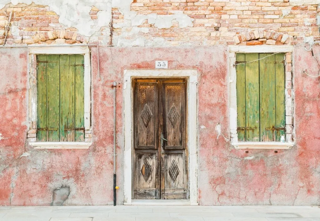 Verfallenes rosa Haus mit Holztür und grünen Fensterläden auf Burano