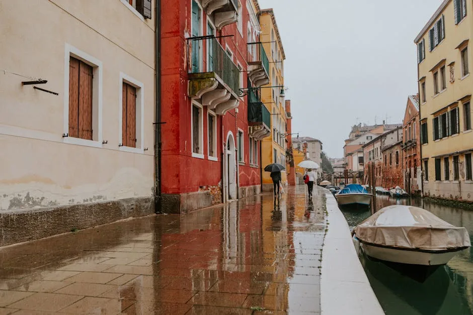Quai pluvieux à Venise, façades colorées et barques amarrées.