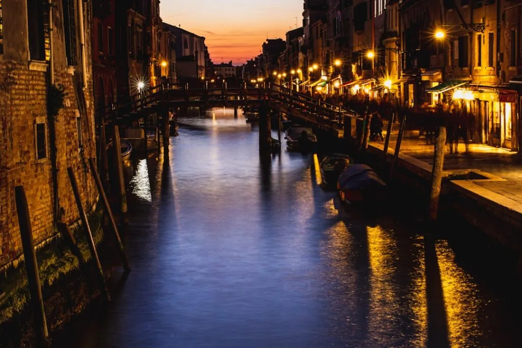 Canal vénitien éclairé la nuit avec ponts et reflets dorés