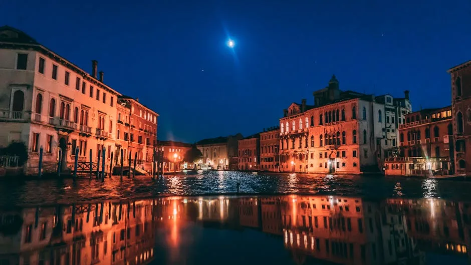 Moonlit Venetian canal reflecting lights from historic buildings at night.