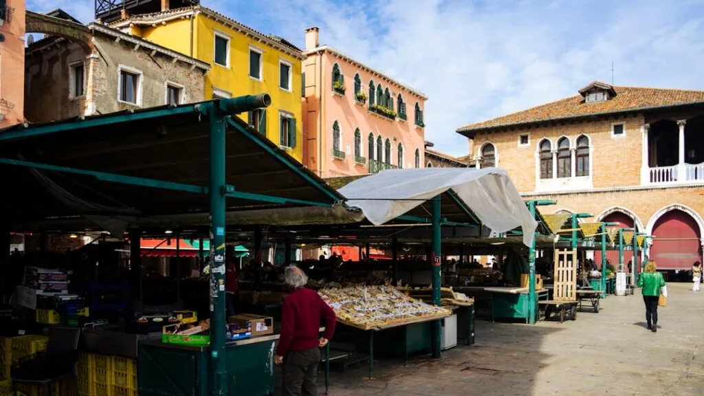 Stands de marché couverts sur une place, façades colorées de Venise.