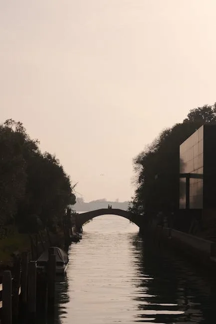 Schmaler Kanal mit Bogenbrücke und zwei Personen im Dämmerlicht in Venedig
