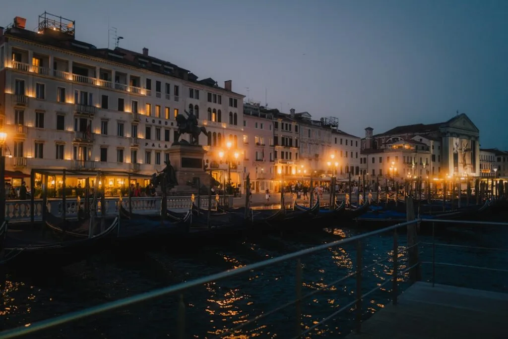 Belebtes venezianisches Ufer bei Nacht, Straßenlaternen an und Gondeln vertäut
