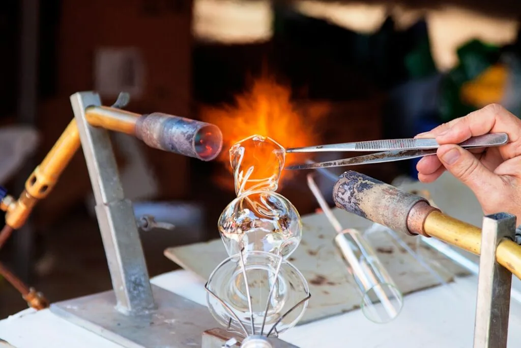 Mains travaillant du verre en fusion au chalumeau, atelier de Murano
