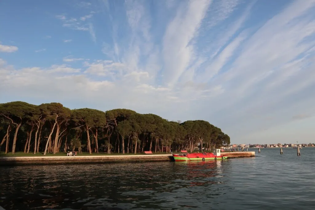 Bateau rouge amarré devant les pins des jardins publics de Venise.