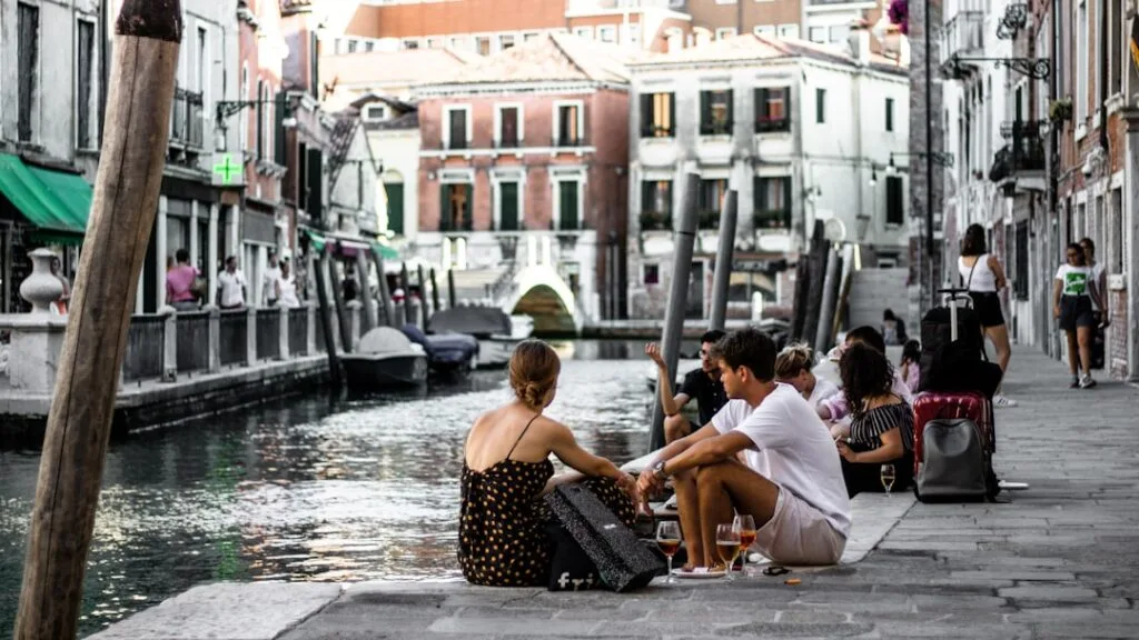 Jeunes assis au bord d'un canal à Venise, apéritifs posés.