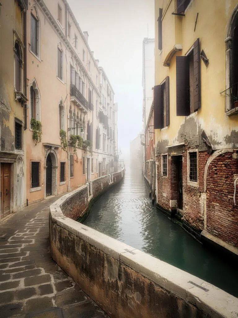 Canal étroit à Venise bordé de bâtiments, passerelle vide sous brume
